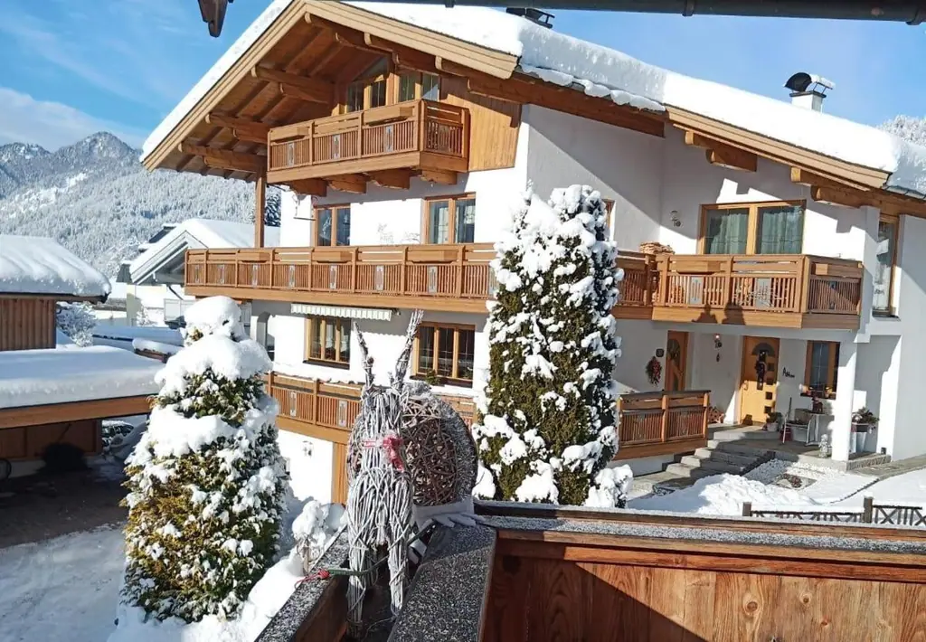 Das tief verschneite Haus bei Sonnenschein, im Vordergrund ein Rentier aus Weidengeflecht, links der Carport