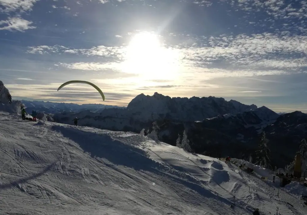 Paragleiter beim Start auf einem verschneiten Berg, dahinter eine Bergkette im Gegenlicht