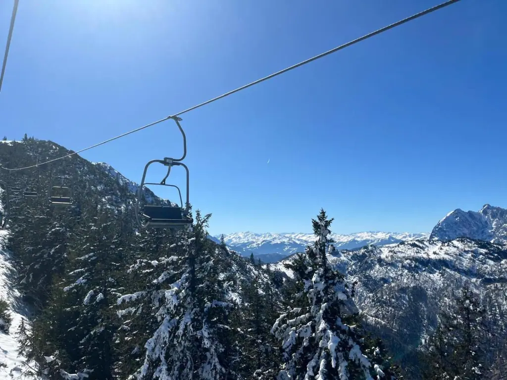 Sessellift über verschneiten Tannen mit weitem Bergpanorama unter blauem Himmel