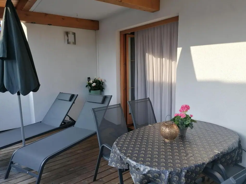 Terrasse mit zwei Sonnenliegen, Sonnenschirm und rundem Tisch mit Geranien