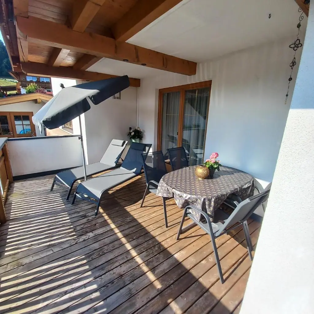 Überdachte Sonnenterrasse mit Holzboden, zwei Liegen, Sonnenschirm und gedecktem Tisch mit Stühlen